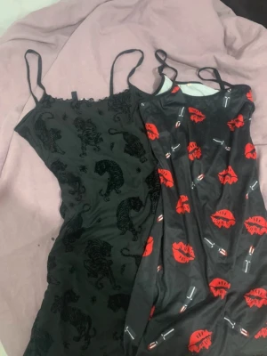 Två svarta nattlinnen med tryck - Säljer två nattlinnen med tunna axelband. Ena är svart med svarta tigrar i sammet, det andra är svart med röda läppar och läppstift-tryck. Båda har figurnära passform och är perfekta för en chill kväll hemma.