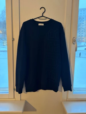 Svart sweatshirt från Burberry - Snygg svart sweatshirt från Burberry med diskret BURR-tryck längs ena sidan framtill. Klassisk rund halsringning och långa ärmar. Perfekt för en clean och stilren look.