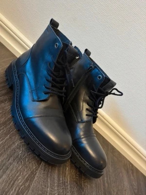 Herr kängor - Ett par svarta kängor från Jack & Jones med snörning framtill och dragkedja på sidan. Skorna har en robust sula. Helt nya, nypris 1499kr