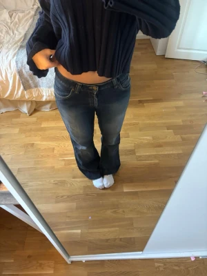Mörkblå bootcut jeans med låg midja - Säljer ett par mörkblå bootcut jeans med låg midja och slitningar på låren. Jeansen har klassiska fem fickor och stängs med knapp och dragkedja. Perfekta för en avslappnad och trendig look. Klippta längst ner