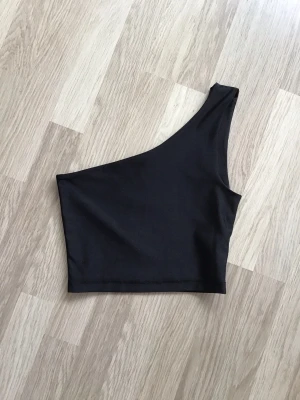 Svart oneshoulder topp från BikBok, stl XS - Snygg svart topp med oneshoulder-design från BikBok. Toppens enkla och stilrena look gör den lätt att matcha med olika outfits. Just nu fri frakt, så du betalar bara för toppen. Jag har fler plagg ute, och hittar du något mer från min garderobsutrensning, så skickar jag allt i samma paket.