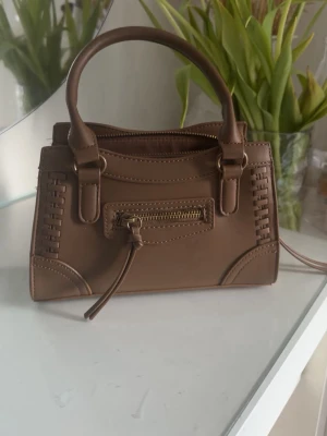 Gina tricot, brun handväska med dragkedja - Snygg brun handväska i rektangulär form med dekorativa sömmar på sidorna och ett litet ytterfack med guldfärgad dragkedja. Gina tricot knappt använd 