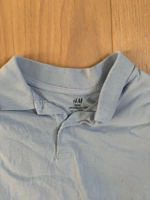 Ljusblå pikétröja  - Snygg ljusblå pikétröja från H&M i mjuk bomull. Klassisk krage och korta ärmar, perfekt till en avslappnad men ändå stilren look. Tillverkad i ekologisk bomull för extra komfort.