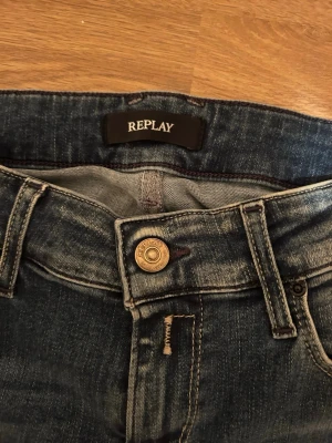 Blå slitna jeans från Replay - Säljer ett par blå jeans från Replay med slitningar och tvättade detaljer för en cool, avslappnad look. Klassisk femficksmodell med knappgylf och smal passform. Perfekta för dig som gillar streetstyle och trendiga outfits.