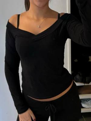 Svart offshoulder topp - Snygg svart offshoulder topp med lång ärm och croppad passform. Toppen har en lätt v-ringad skärning och sitter tight mot kroppen, perfekt för att skapa en trendig och stilren look.