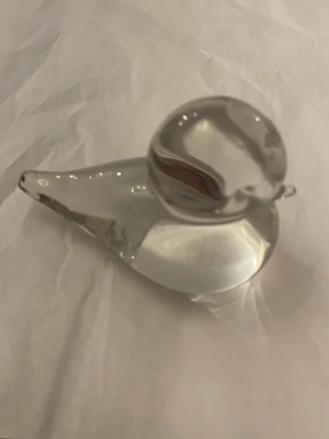 Glasfågel prydnad - Säljer en stilren glasfågel i transparent glas. Fågeln har rundad kropp och huvud med en liten näbb, perfekt som dekoration i hemmet eller som samlarobjekt. Passar snyggt i bokhyllan eller på skrivbordet.