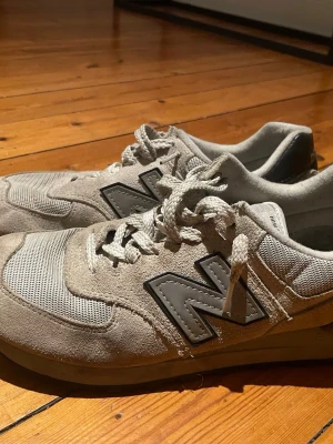 Beige New Balance sneakers i mocka - Stilrena beige sneakers från New Balance med stora svarta N-loggor på sidorna. Skorna har ovandel i mocka och mesh för extra andningsförmåga, samt vita snören. Klassisk låg modell som funkar till det mesta.