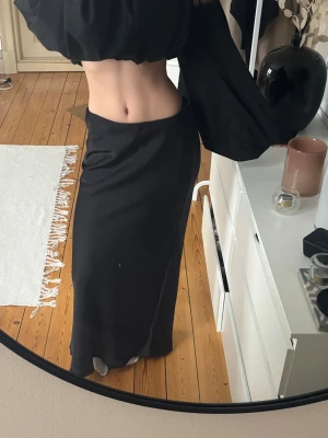 Svart långkjol i satin-look - Säljer en svart långkjol med slät och glansig satin-look. Kjolen har en rak passform och sitter högt i midjan. Perfekt att styla med crop tops eller stickade tröjor för en clean och trendig vibe.