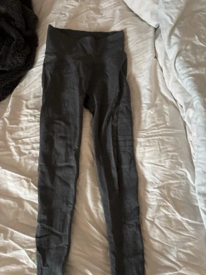 Mörkgrå ribbade seamless tights - Säljer ett par mörkgrå tights från Amin med ribbad struktur och hög midja. De är seamless för extra komfort och har en tight passform som framhäver benen. Perfekta för träning eller chill dagar. Materialet känns stretchigt och mjukt.