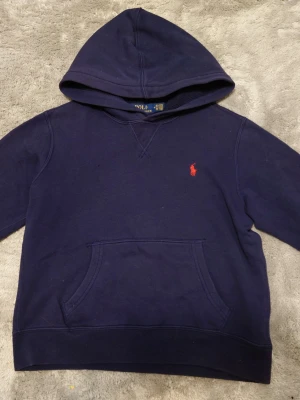 Mörkblå hoodie från Polo Ralph Lauren - Mörkblå hoodie från Polo Ralph Lauren. Tröjan är i storlek M10-12. Riktigt fint skick 9/10. Bara att höra av sig för fler frågor! .