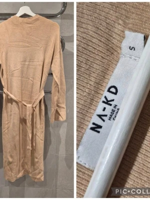 Beige klänning från NA-KD - Mysig beige morgonrock från NA-KD i mjukt stickat material. Modellen har långa ärmar och ett matchande knytband i midjan för en avslappnad look. Perfekt för chilliga morgnar eller kvällar hemma.