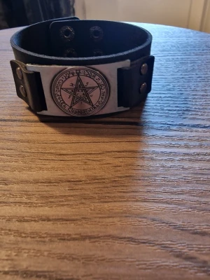 Armband vintage pentagram - Svart läderarmband med ett detaljerat pentagram i metall. Armbandet har justerbara tryckknappar för att passa olika handledsstorlekar. Storlek 23 cm långt. Bredd 3 cm.