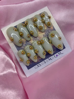 Dune (XL);Medium Almond - Snygga handgjorda press-on naglar i en mjuk grön nyans med koreansk vit blush design. Varje nagel är dekorerad med guldfärgade metallpärlor för en unik och trendig look. Formen är medium almond. Perfekt för dig som vill sticka ut.XL: 17 mm, 13 mm, 14 mm, 12 mm, 11 mm 