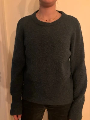 Mörkgrön stickad tröja - Mysig mörkgrön stickad tröja med rund halsringning och långa ärmar. Tröjan har en enkel, rak passform och är tillverkad i ett mjukt, fluffigt material som känns skönt mot huden. Perfekt för kyliga dagar och enkel att matcha med olika outfits.