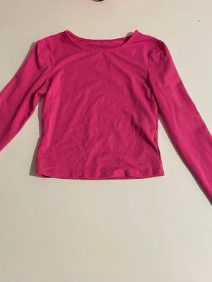 Rosa långärmad topp - En enkel och snygg rosa långärmad topp med rund hals. Toppen har en rak passform och är tillverkad i mjukt bomullstyg, perfekt att matcha med jeans eller kjol för en avslappnad look.