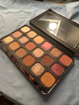 Ögonskuggspalett med varma toner - Snygg ögonskuggspalett med 18 olika nyanser i varma och neutrala färger, både matta och skimrande. Färgerna går i guld, koppar, brunt, rosa och nude. Paletten har spegel i locket och fyrkantiga pans. Perfekt för kreativa sminkningar och trendiga looks. Använd ett par gånger