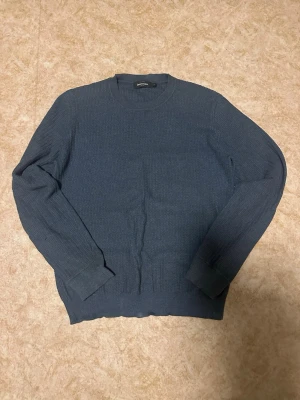 Mörkblå stickad tröja Uniqlo - Mörkblå stickad tröja från Uniqlo med rund halsringning och långa ärmar. Tröjan har en enkel, stilren design och ribbade muddar vid ärmslut och nederkant. Perfekt för dig som gillar minimalistisk stil.