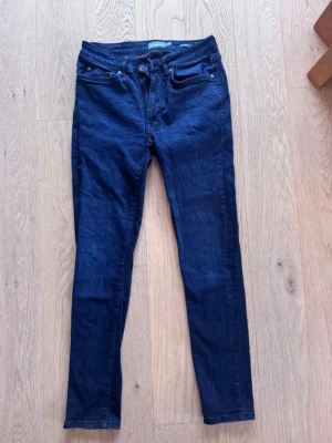 Mörkblå skinny jeans som nya - Snygga mörkblå skinny jeans med klassisk femficksdesign och läderpatch bak i midjan. Jeansen har smal passform och är tillverkade i ett mjukt denimtyg som sitter skönt. Perfekta för dig som gillar en enkel och stilren look. W29/L30, som nya!