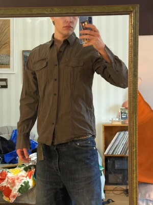 Skjorta från iDentity 100% bomull  - Säljer en grön/brun skjorta från iDentity med klassisk krage och knappar framtill. Skjortan har två bröstfickor. Skjortan är storlek M och i 100% bomull. 