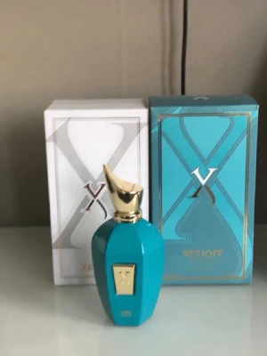 Xerjoff turkos parfymflaska - Lyxig parfym från Xerjoff i en elegant turkos flaska med gulddetaljer och unik form. Kommer i exklusiv förpackning med färgstark insida och matchande ytterkartong. Perfekt för dig som gillar exklusiva dofter och snygg design.