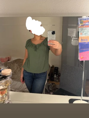 Grön kortärmad blus från B.young - Söt grön blus från B.young med korta puffärmar och rundad halsringning med knyt. Blusen har små diskreta prickar i tyget och elastiska detaljer vid ärmslut och nederkant. Perfekt för en avslappnad och trendig look.