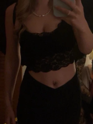 Svart spetsig croppad linnetopp - Snygg svart croppad linnetopp med spetsdetaljer och tunna axelband. Toppen har en feminin och trendig look med blommönstrad spets och vågig kant nertill. Perfekt att styla till höga jeans eller kjol. Bara använd några gånger. I storlek S.💞