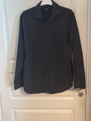 Svart klassisk skjorta - Stilren svart skjorta med klassisk krage och knappar framtill. Skjortan har lång ärm och en rak passform som funkar till många olika looks. Perfekt för dig som gillar en enkel och clean stil.
