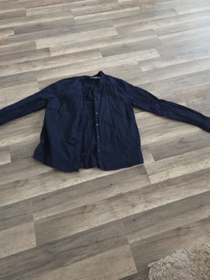 Mörkblå skjorta med knappar - Stilren mörkblå skjorta med lång ärm och knäppning framtill. Skjortan har en klassisk passform och är tillverkad i ett lätt bomullstyg som känns skönt mot huden. Perfekt för dig som gillar en enkel och clean look.