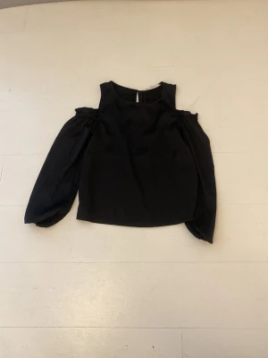 Svart offshoulder topp med puffärm - Trendig svart topp med offshoulder-design och långa puffärmar. Toppen har en rak passform och är perfekt för dig som vill ha en stilren men ändå cool look. Materialet känns mjukt och lätt mot huden.