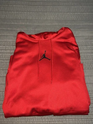 Röd Jordan hoodie med huva - Snygg röd hoodie från Jordan med klassisk Jumpman-logo på bröstet. Hoodien har en stor huva med dragsko och en praktisk magficka. Materialet är mjukt och känns skönt mot huden, perfekt för dig som gillar sportig och avslappnad stil.