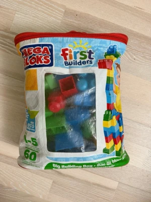 Mega Bloks First Builders byggklossar - Säljer en påse Mega Bloks First Builders byggklossar i olika färger som blå, röd, grön och gul. Klossarna är stora och kommer i en praktisk förvaringsväska med dragkedja. Perfekt för kreativ lek och byggande för yngre barn.
