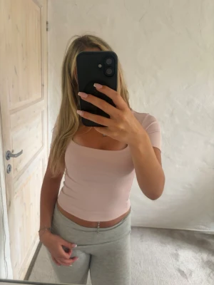 Ljusrosa croppad topp med kort ärm - Säljer en ljusrosa croppad topp med korta ärmar och fyrkantig ringning. Toppen har en tight passform och är tillverkad i ett mjukt, stretchigt material som sitter snyggt på kroppen. Perfekt att matcha med höga byxor eller kjol.