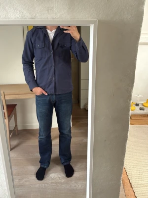 Mörkblå overshirt  - Stilren mörkblå overshirt från John Henric med raka linjer och klassisk krage. Två bröstfickor med knappstängning och två sidofickor. Tillverkad i ett mjukt bomullstyg som ger en avslappnad men snygg look. Perfekt att bära året om, den är vattentålig.