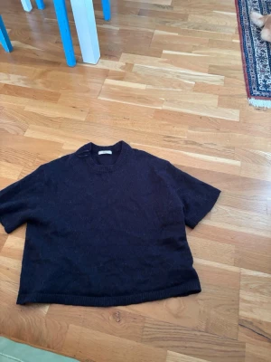 Svart stickad tröja från Gina tricot - Mysig svart stickad tröja från Gina tricot med rund halsringning och ribbade muddar. Enkel och stilren design som passar perfekt till alla outfits. Tröjan är i ett mjukt material och har korta ärmar.