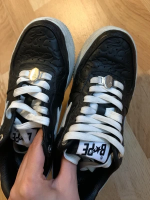 Svarta BAPE STA sneakers med vit sula - Säljer ett par svarta BAPE STA sneakers i läder med vit sula och vita detaljer. Skorna har präglat mönster på ovandelen, vita skosnören och den ikoniska stjärnan på sidan. Klassisk streetwear-vibe och tydlig BAPE-logga på hälen.