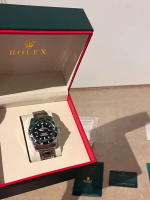 Role Submariner klocka silver/svart - Säljer en stilren Role Submariner med svart urtavla och grön vridring. Klockan har ett klassiskt armband i silverfärgat stål och levereras i originalbox med tillhörande certifikat och dokumentation. Perfekt för dig som gillar exklusiva accessoarer.