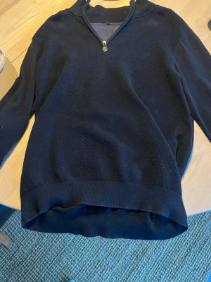 Mörkblå ziptröja från Less Worries - Mörkblå tröja från Less Worries med halv dragkedja framtill. Tröjan har en diskret struktur i materialet, ribbade muddar vid ärmslut och nederkant samt en klassisk, avslappnad passform. Perfekt för lager på lager och enkel att matcha med jeans eller chinos.