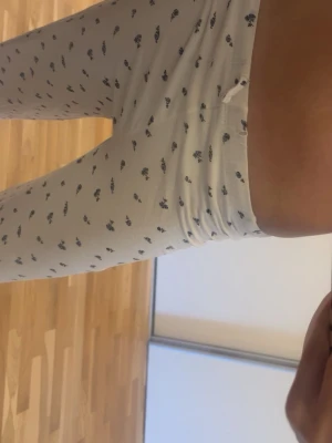 Vita pyjamasbyxor med blommönster - Mysiga vita pyjamasbyxor med små blå blommor över hela tyget. Byxorna har rak passform och resår i midjan med en liten rosett framtill. Perfekta för chillkvällar hemma och gjorda i mjukt material som känns skönt mot huden.