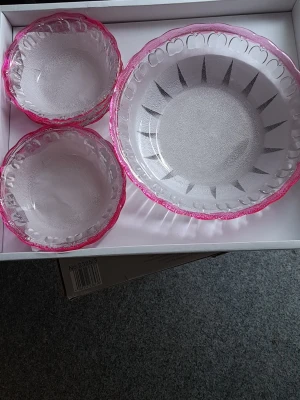 Helt nya.  Glasskålset med rosa kant - Helt nya. Säljer ett set med glasskålar i transparent glas med dekorativ rosa kant. Setet innehåller en större serveringsskål och flera mindre skålar, perfekta för dessert eller snacks. Skålarna har ett mönster längs kanten och är både snygga och praktiska till köket.