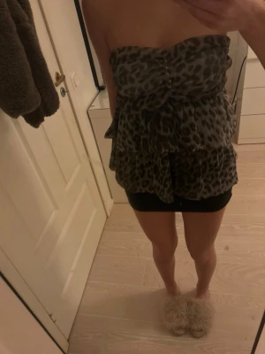 Leopardmönstrad bandeau topp Trols KA - Säljer en bandeau topp från Trols KA med leopardmönster i grå och svarta toner. Toppen är axelbandslös, har volangdetaljer och knappar framtill. Perfekt för fest! Säljer för att den är för stor för mig. Förra ägaren har sytt in den och det går att enkelt sprätta upp men skulle säga att den passar en större byst S eller M. kan även passa större om man sprättar💗
