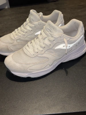 Saucony 3D grid hurricane vita mesh och mocka sneakers - Snygga vita sneakers från Saucony med ovandel i mesh och mocka. Skorna har klassisk låg siluett, vita snören och Saucony-logga på sidan. Perfekta för en clean och sportig look. Sulan är vit med svart yttersula för extra kontrast.