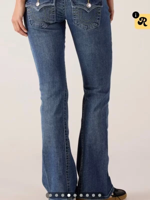 Blå bootcut jeans från True Religion - Säljer ett par blå bootcut jeans från True Religion med klassiska kontrastsömmar och snygga fickdetaljer bak. Jeansen har låg midja och utsvängda ben, tillverkade i mjuk denim med stretch för extra komfort. säljer då de blivit för stor på mig och behöver en mindre storlek. köpt för 1400kr