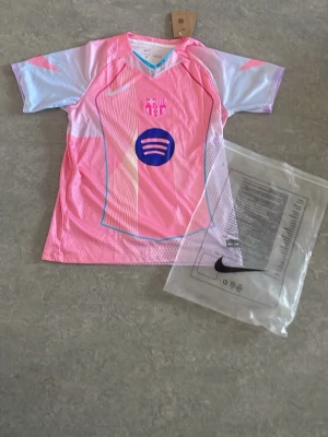 Barça rosa matchtröja Nike - Snygg rosa FC Barcelona matchtröja från Nike med klubbmärke och Spotify-logga på bröstet. Tröjan har korta ärmar, sportig passform och är tillverkad i lätt, ventilerande funktionsmaterial. Perfekt för fotbollsträning eller att bära som supporter.