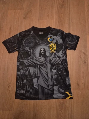 Svart Brasilien t-shirt med tryck - Brazil svart t-shirt med stort tryck av Kristusstatyn och detaljerade grafiska mönster. Gult och blått Brasilien-emblem på bröstet och ryggen och är köpt i Brasilien. Och är bara använd 1 gång.