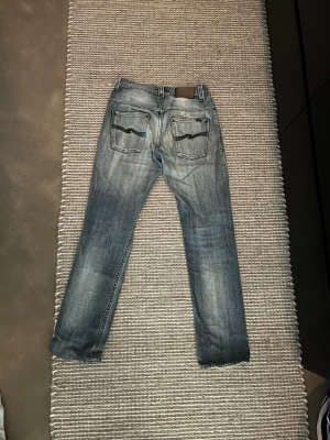 Blå slitna jeans med raka ben - Säljer ett par blå jeans med slitningar och raka ben. Jeansen har klassisk femficksdesign och snygga detaljer på bakfickorna. Materialet är denim med tvättad look och lätt slitna partier framtill för en trendig vibe.