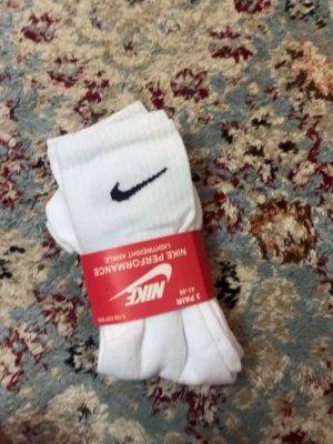 Vita Nike strumpor 3-pack - Säljer ett 3-pack klassiska vita strumpor från Nike med svart logga på sidan. Strumporna är ribbade och tillverkade i mjuk bomullsblandning för skön passform. Perfekta till sneakers och sportiga outfits.