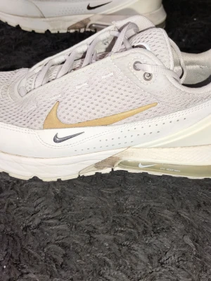Nike Air Max 270 vita sneakers - Nike Air Max 270 sneakers i vitt med mesh-överdel och detaljer i beige och svart. Skorna har synlig Air Max-dämpning i hälen och flera Swoosh-loggor på sidorna. Låg modell med snörning och ventilerande material för extra komfort. Storlek 41. Skorna är i bra skick.