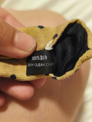 Prickig slips i siden från A. Christensen - Säljer en gul slips i 100% siden från A. Christensen med svarta prickar. Märket är broderat på baksidan och slipsen har en klassisk form. Perfekt för dig som vill addera lite färg och mönster till din outfit.