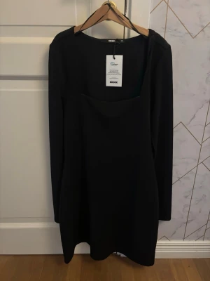 Svart långärmad klänning Bik Bok - Stilren svart klänning från Bik Bok med lång ärm och fyrkantig ringning. Kort modell som passar perfekt till många tillfällen. Tillverkad i ett mjukt material som ger en bekväm passform.