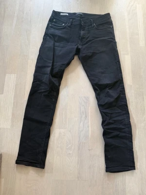 Svarta slim fit jeans Jack & Jones - Snygga svarta slim fit jeans från Jack & Jones, modell Glenn. Klassisk femficksdesign med dragkedjegylf och metallknapp. Jeansen har en smal passform och är tillverkade i stretchigt material för extra komfort.